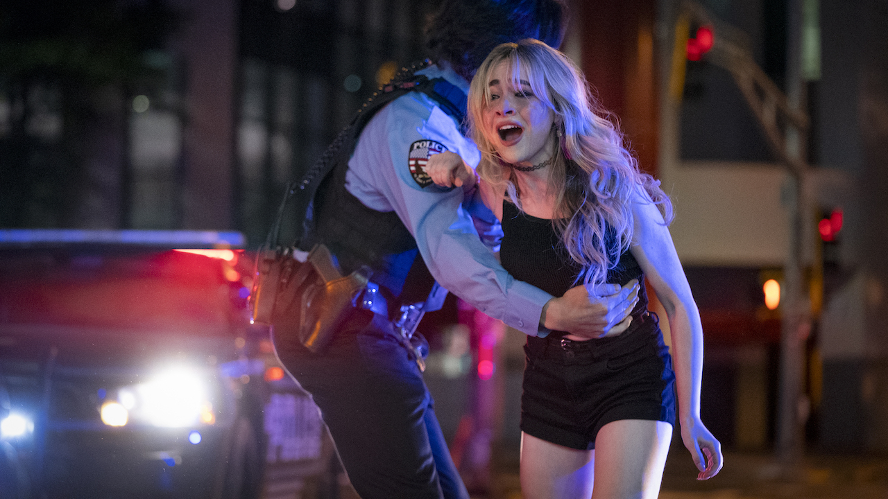 Sabrina Carpenter being pulled back by the police in Emergency 2022 film