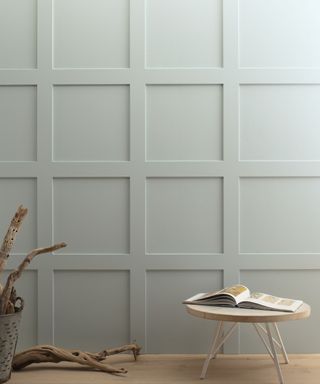 light gray panelled wall, wooden floor with low round wood table with opened book