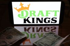 DraftKings logo on a smartphone reflected on table top with five dollar bills