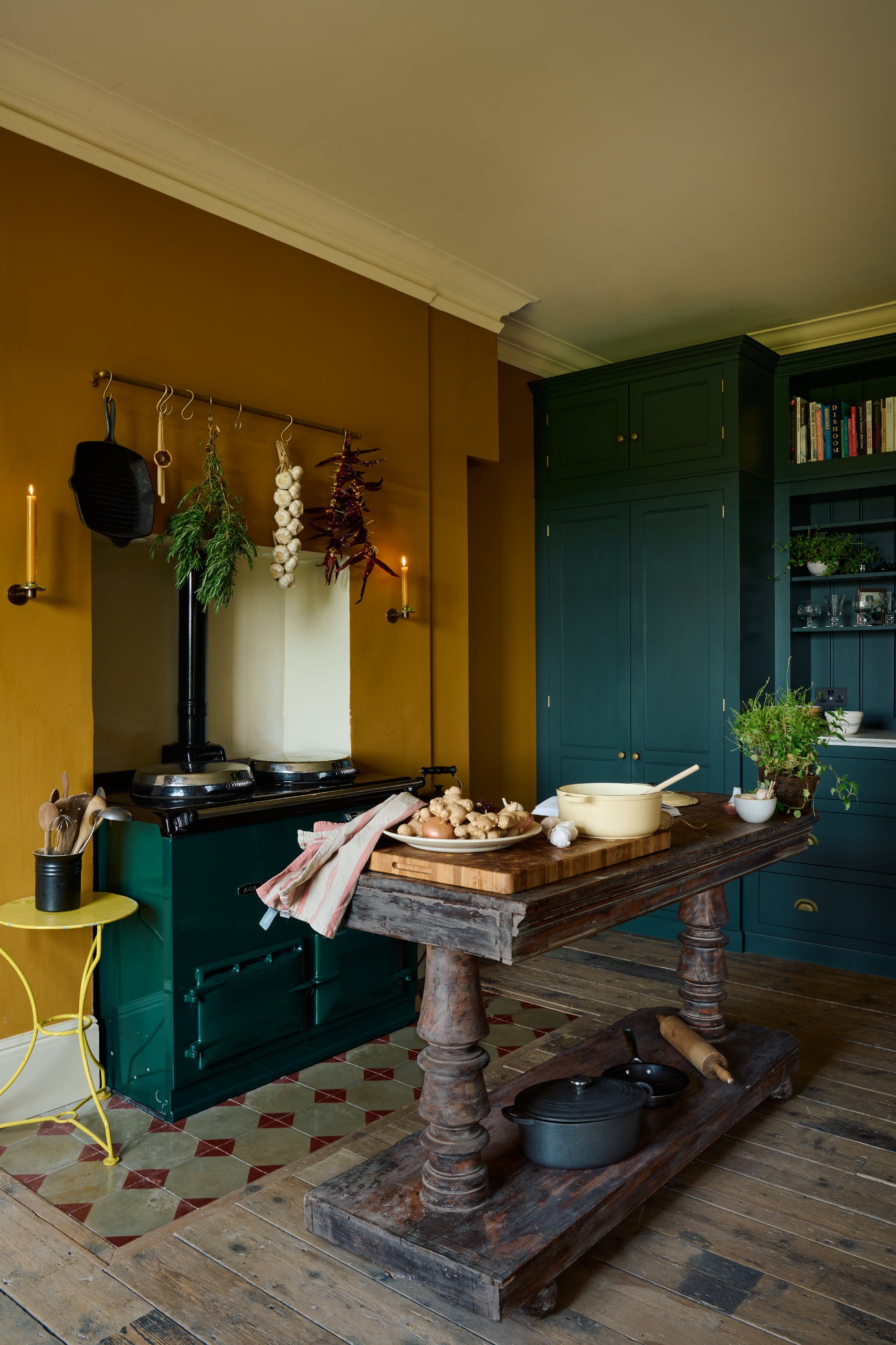 A traditional kitchen in yellow and teal with an antique wood island and candlelit sconces either side of the range cooker