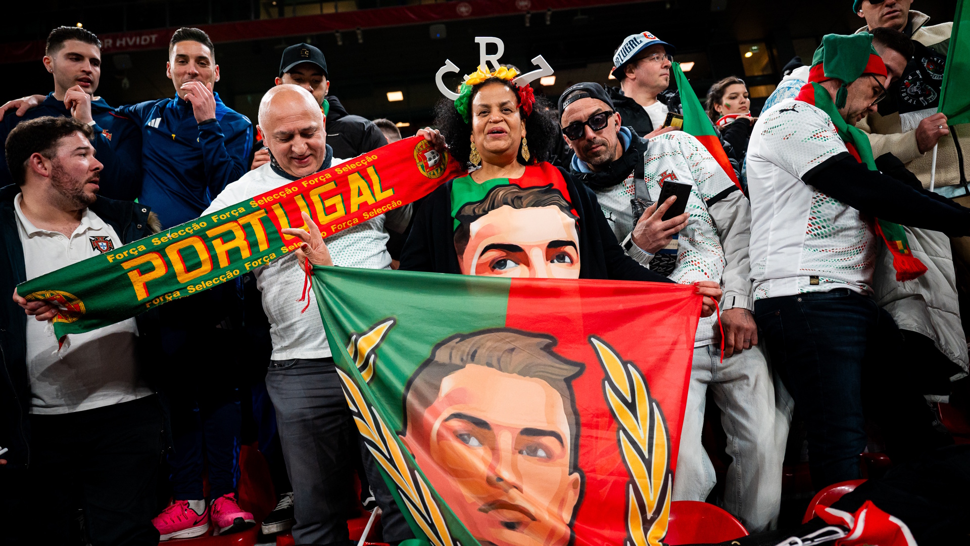 Woman seen wearing a CR7 - Cristiano Ronaldo shirt and holds flag with his portrait while surrounded by other soccer fans during a Portugal match.