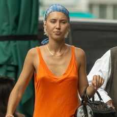 Iris Law walks down the street wearing an orange tank top with long-line shoes, flip-flops and a bandana.