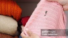 Person holding pink sweater with holes in in front of pile of folded sweaters