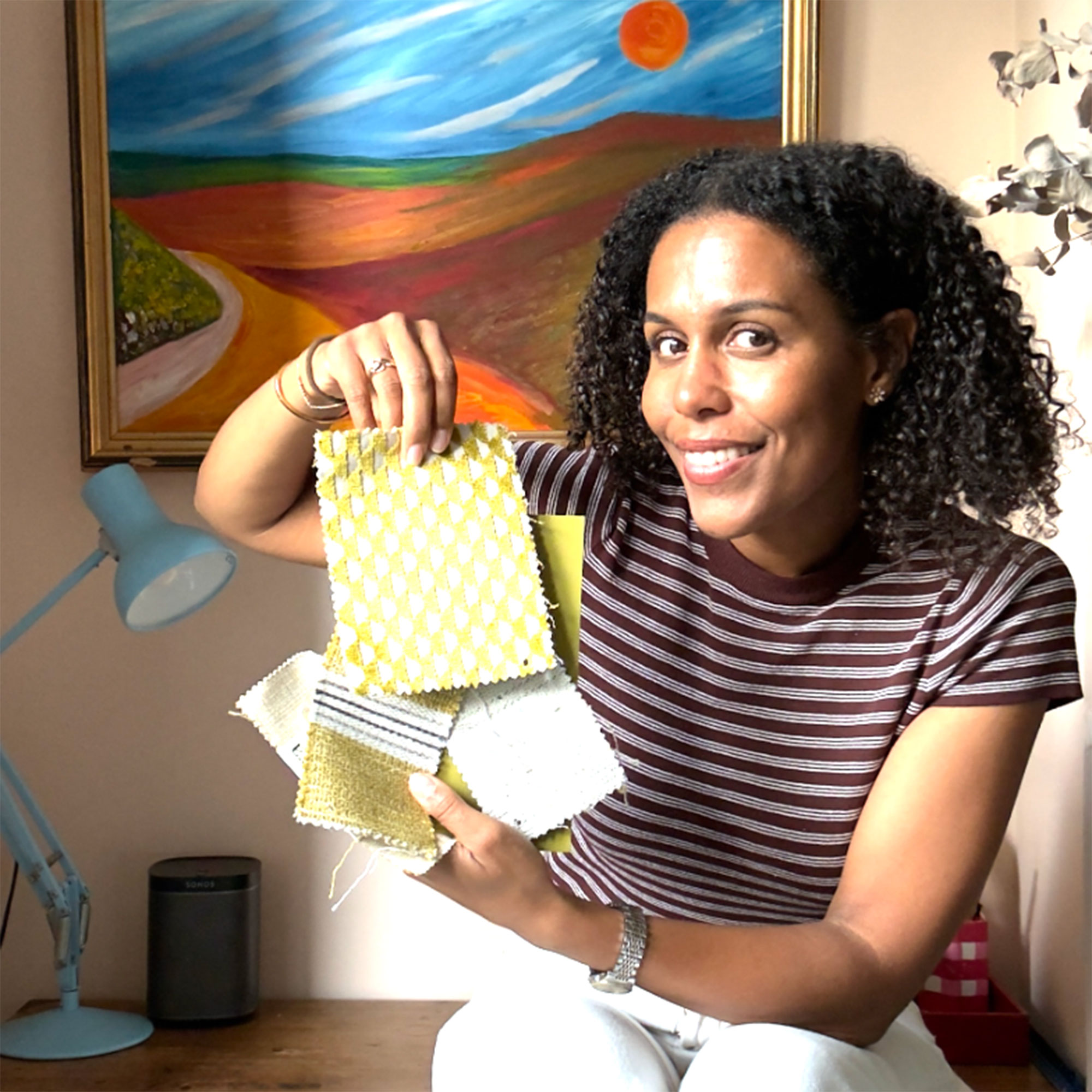 Woman in striped top holding up fabric samples in front of painting of landscape