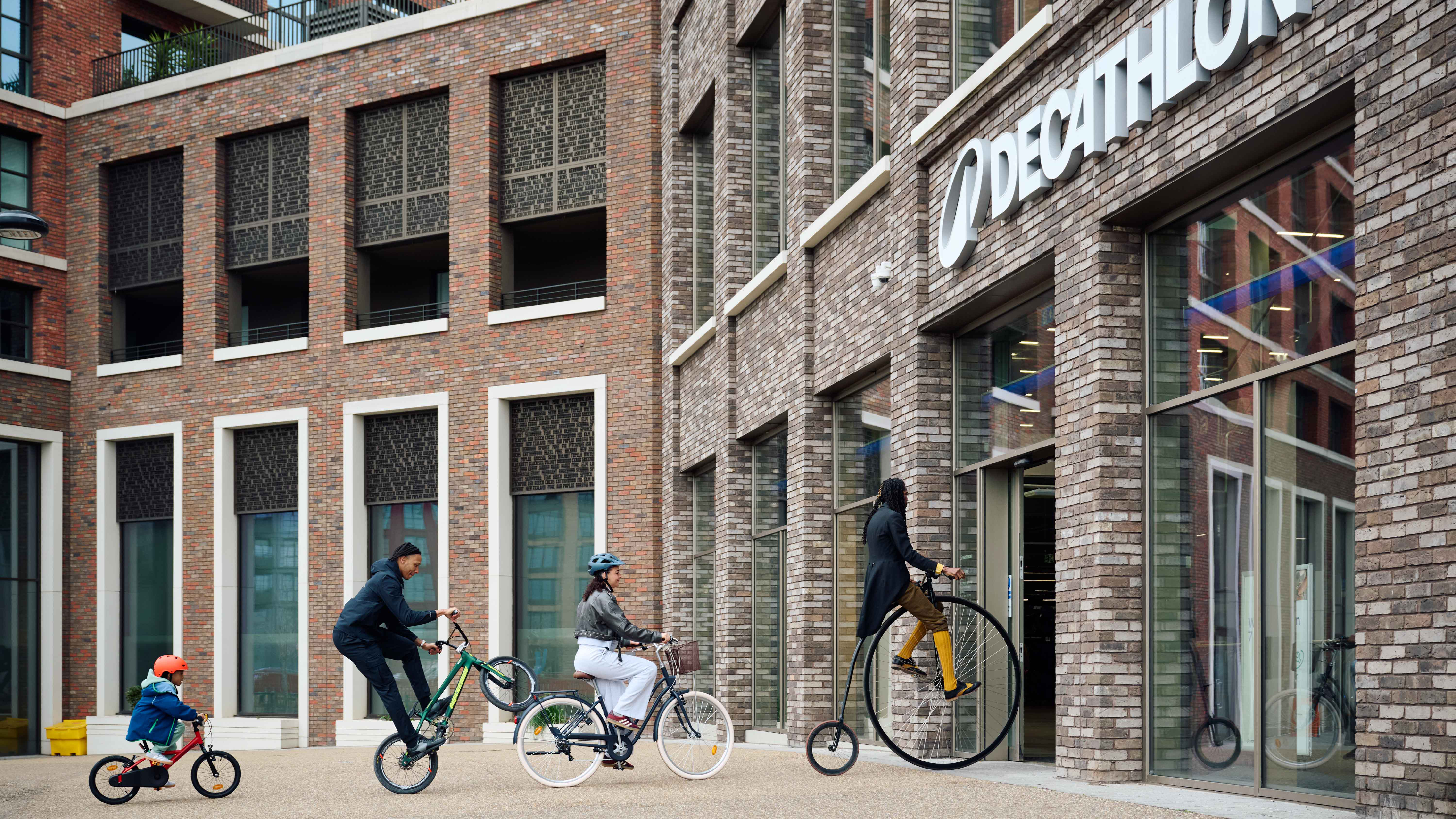 A child, BMXer, lady on a classic style bike and gentlemen on a penny farthing riding into a Decathlon store