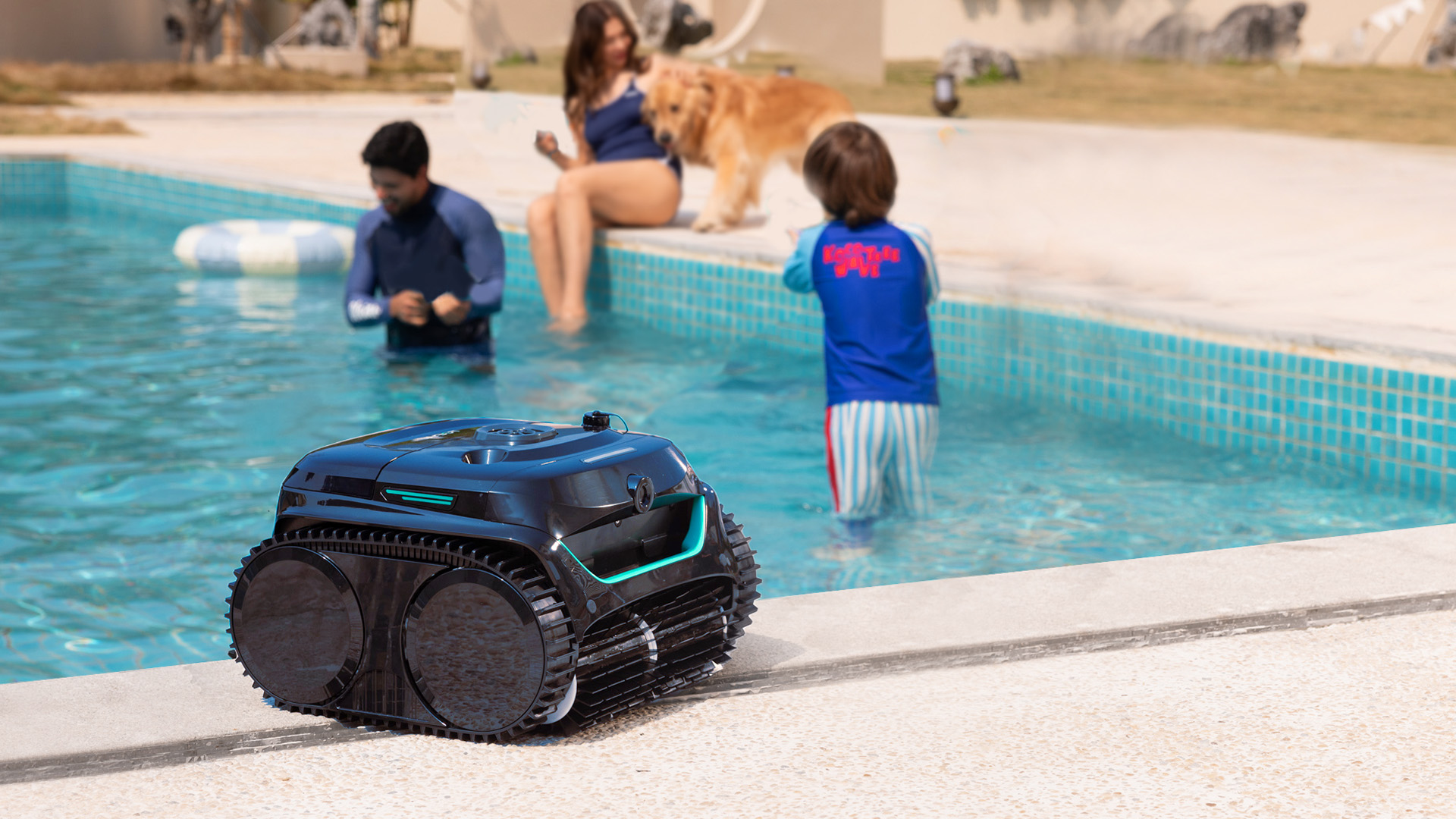 A WYBOT C2 Vision pool cleaner sits beside a large mosaic tile pool while a family enjoys the water in the background.