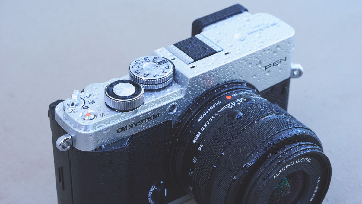 Top half of the OM System PEN camera and it's covered in water droplets