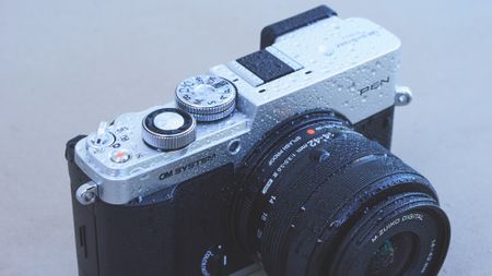 Top half of the OM System PEN camera and it's covered in water droplets