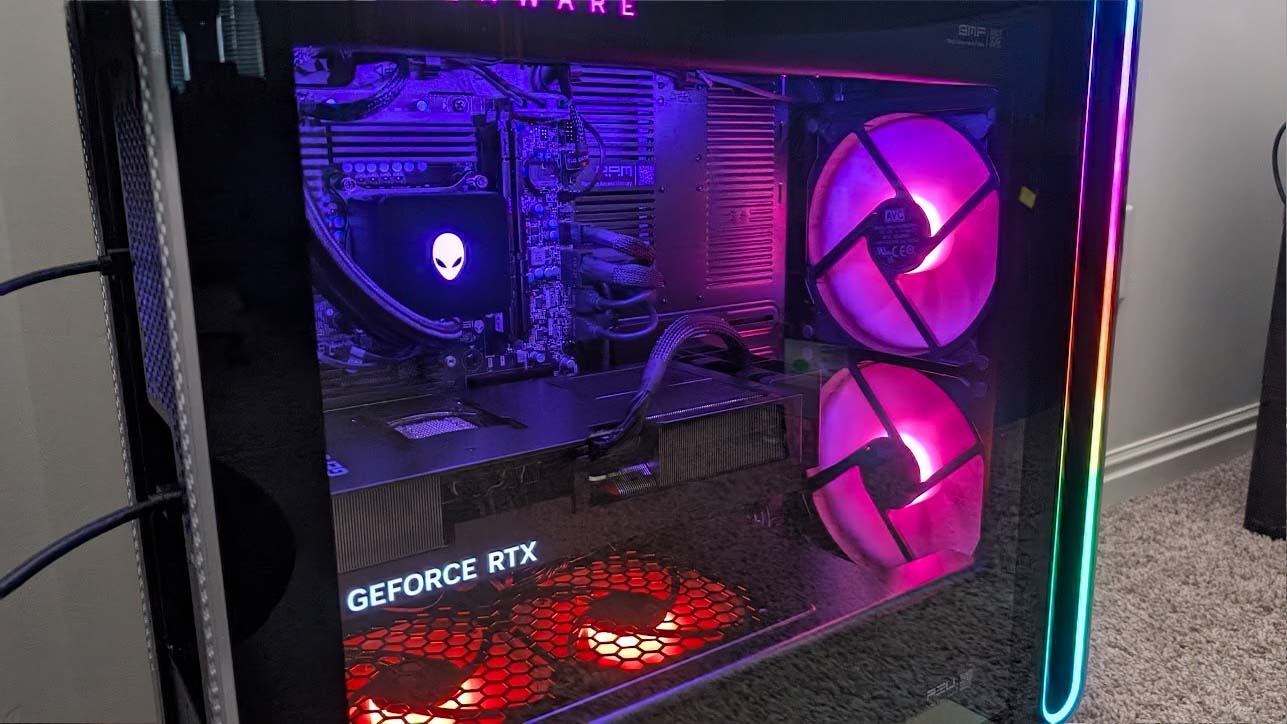 Edited image of the Alienware Area-51 Desktop with RGB lighting highlighting fans, GPU, and other internals. Distracting reflections on the glass have been removed.