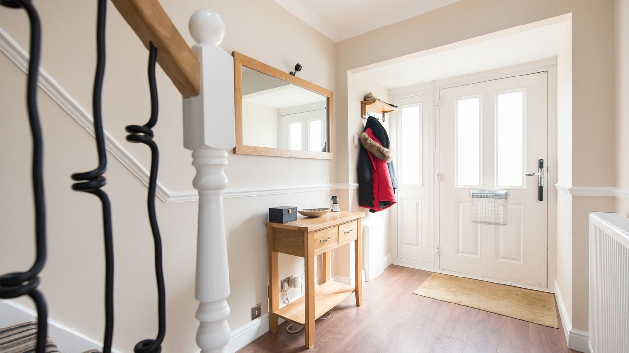 Bright entryway with mirror, table, hanging coats, stairs and white front door - for article on all the places you&#039;re probably forgetting to clean in your entryway