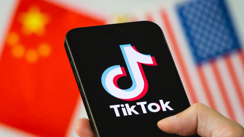 A person holds a phone with the TIkTok logo on the screen with US and China flags in the background