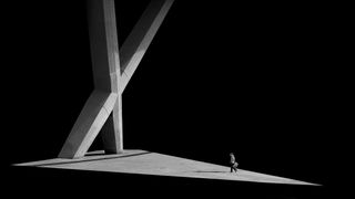 Person walking under a large concrete structure casting a shadow, in black and white