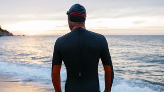 A man wearing a wetsuit looks out to sea