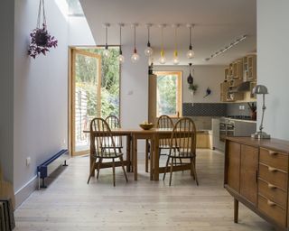 A kitchen with a traditional wooden cabinet and dining table with exposed-bulb pendant ceiling lights