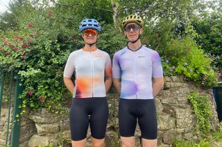 A male and female wearing the unisex Santini Ombra cycling jersey with a stone wall and greenery in the background