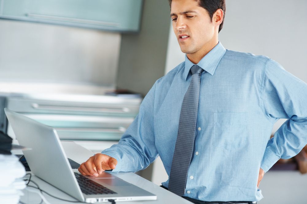 A man sits at his desk, grimacing in pain.