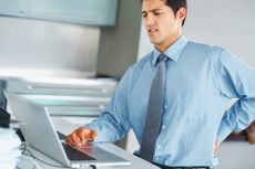 A man sits at his desk, grimacing in pain.
