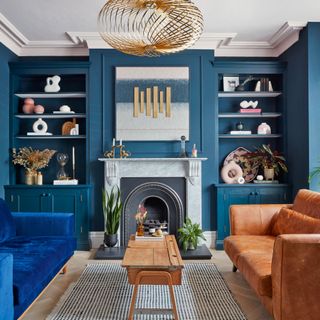 Living area with dark blue painted walls, one blue sofa and one tan leather