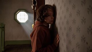 A boy presses his ear to a wall 