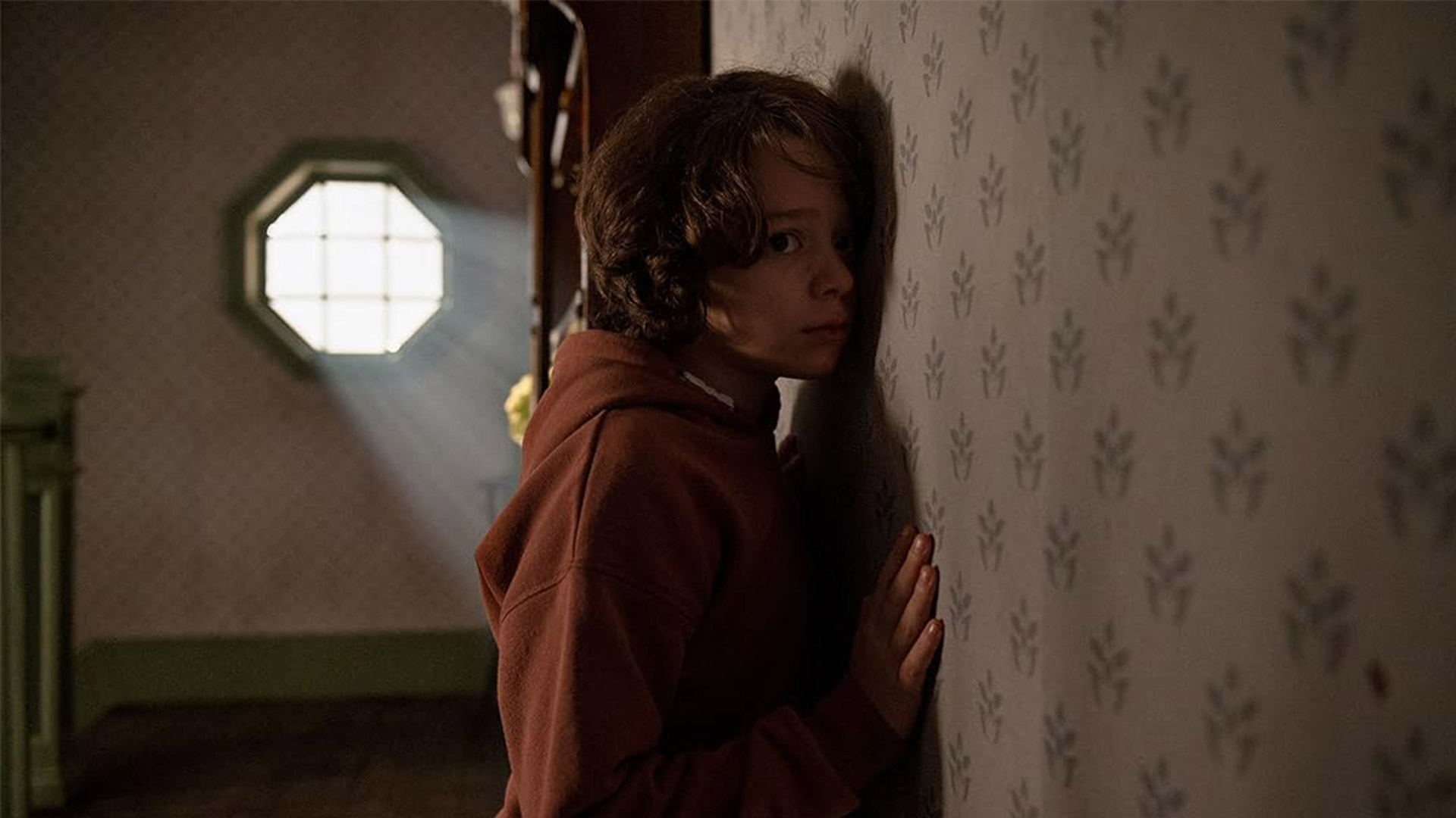 A boy presses his ear to a wall 