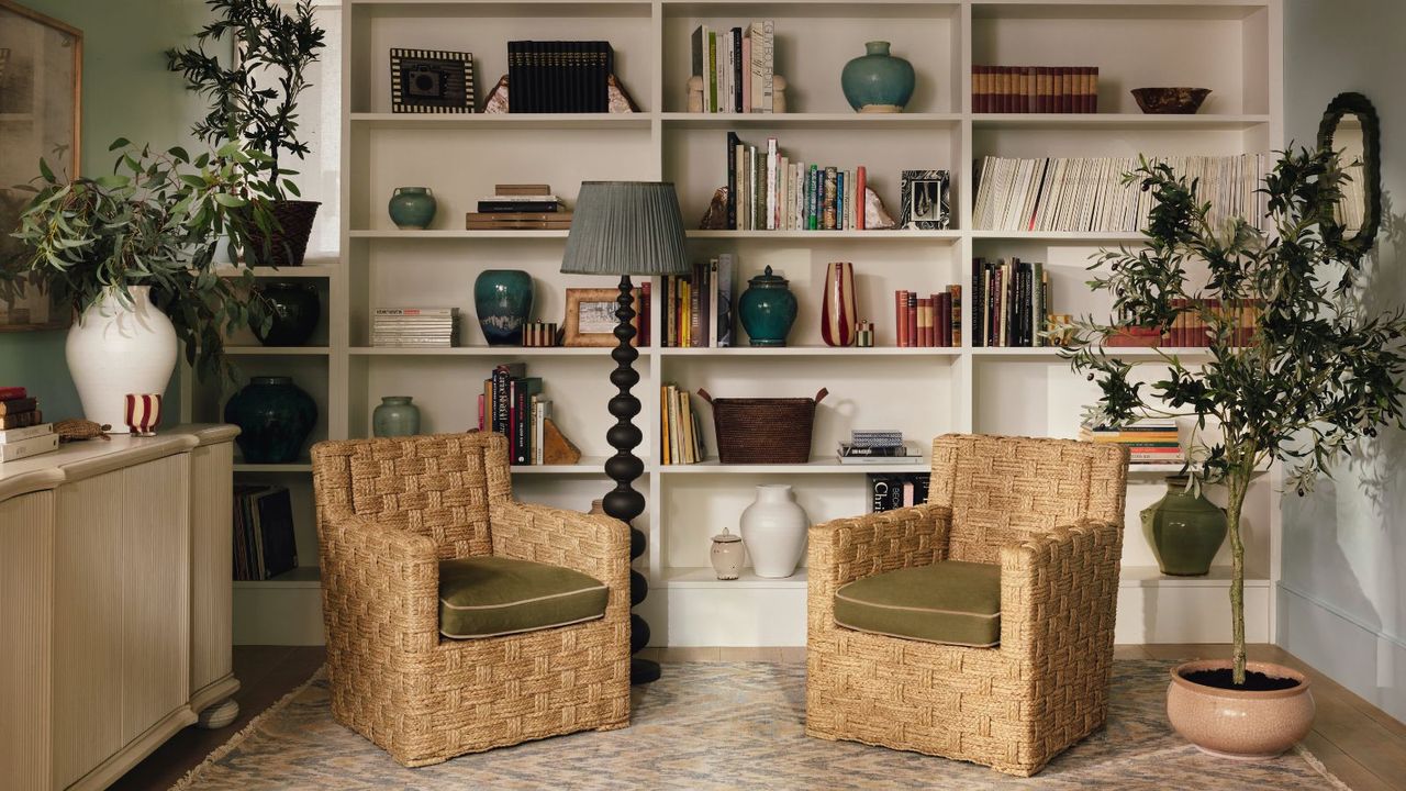 A living room with floor-to-ceiling white bookshelves behind two rattan wicker arm chairs with green cushions. 