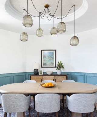 A dining room with blue paneling and a sculptural chandelier hanging from an alcove in the ceiling