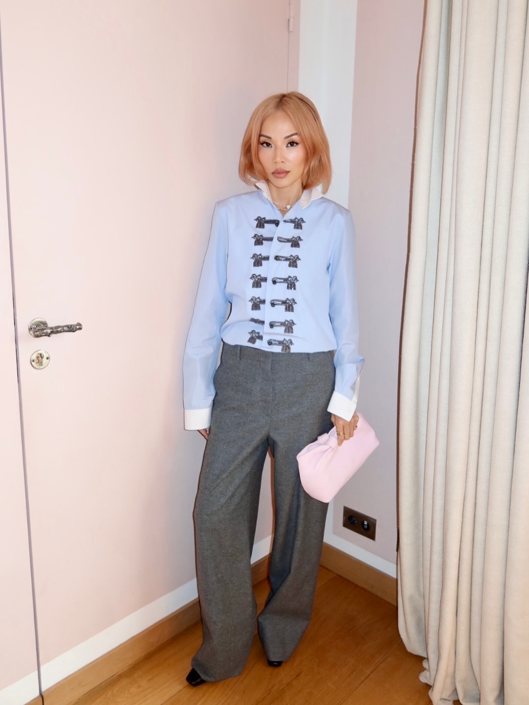 woman posing in front of a door wearing a baby blue military jacket with grey pants