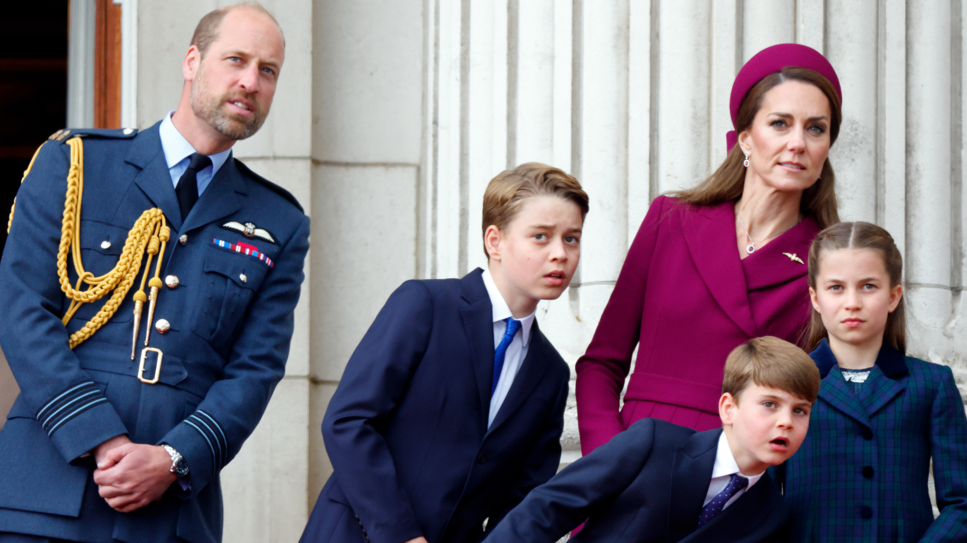 Prince George, Princess charlotte, Prince Louis, Kate Middleton and Prince William leaning to the right looking at planes from the palace balcony