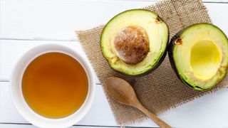 honey and a halved avocado on a table with a wooden spoon