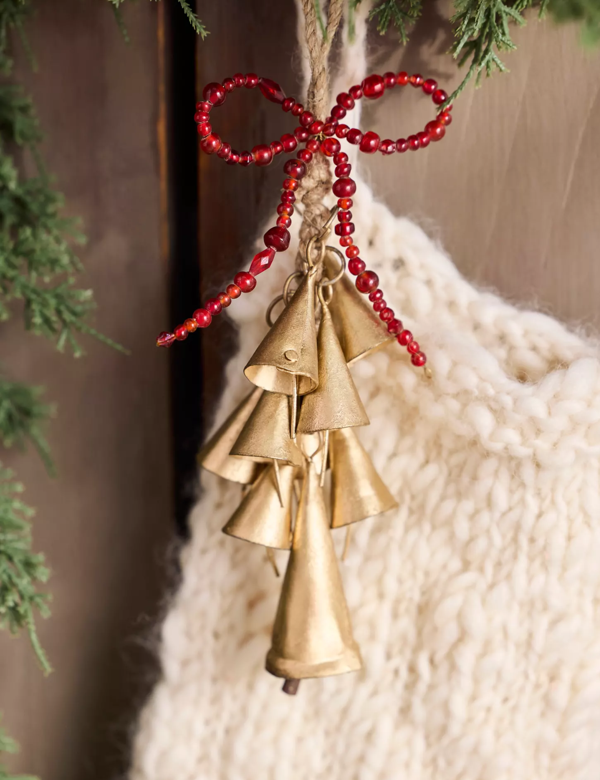 Bell-cluster Christmas charm hanging from a cream knitted stocking against a rust wooden background