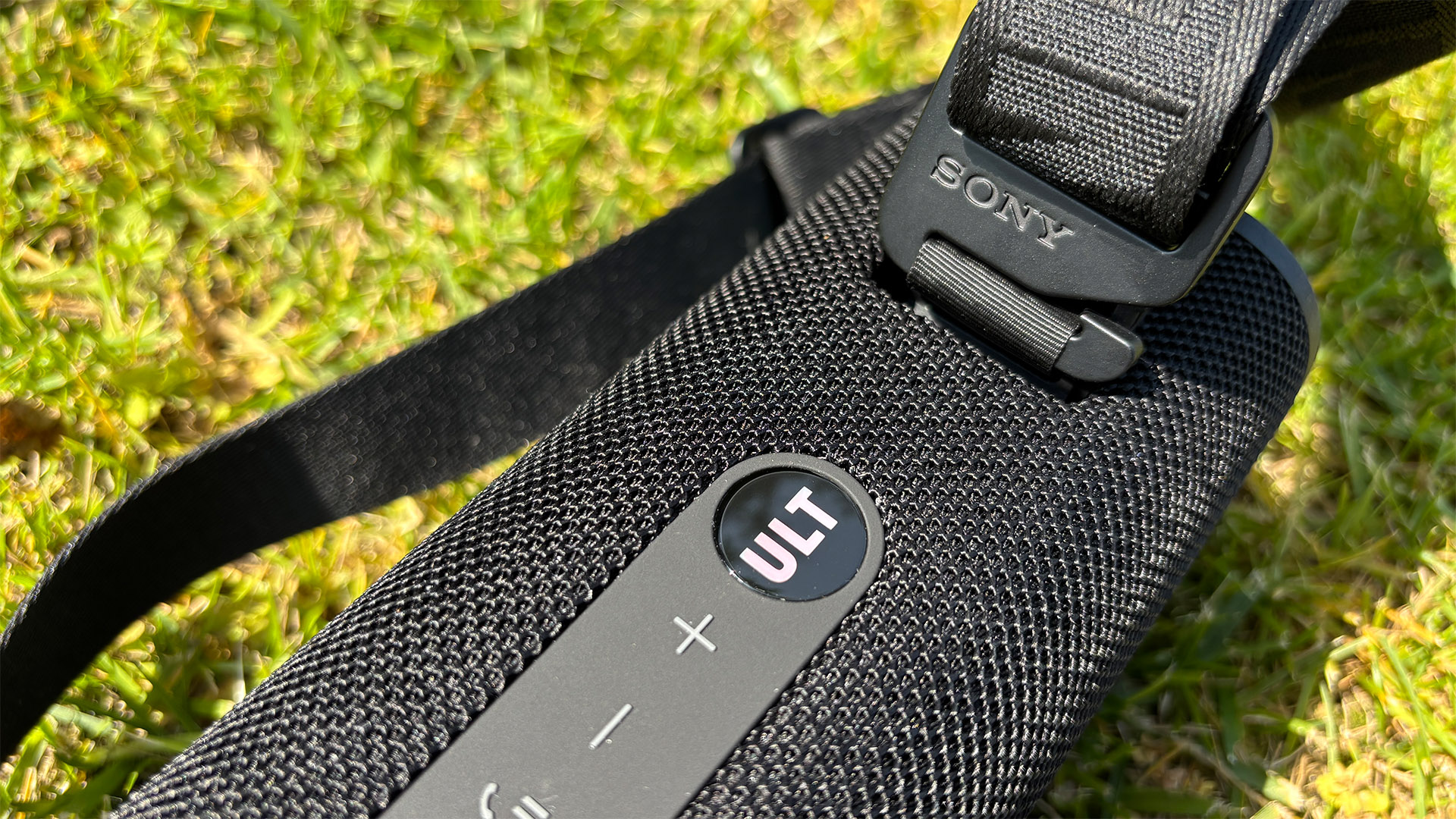 Sony ULT Field 3 wireless speaker on grassy lawn close up on ULT button and carry strap