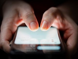 A person holding a mobile phone with their thumbs hovering over the screen