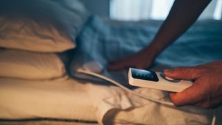 A man adjusting the settings on his electric blanket on a made bed in low lighting