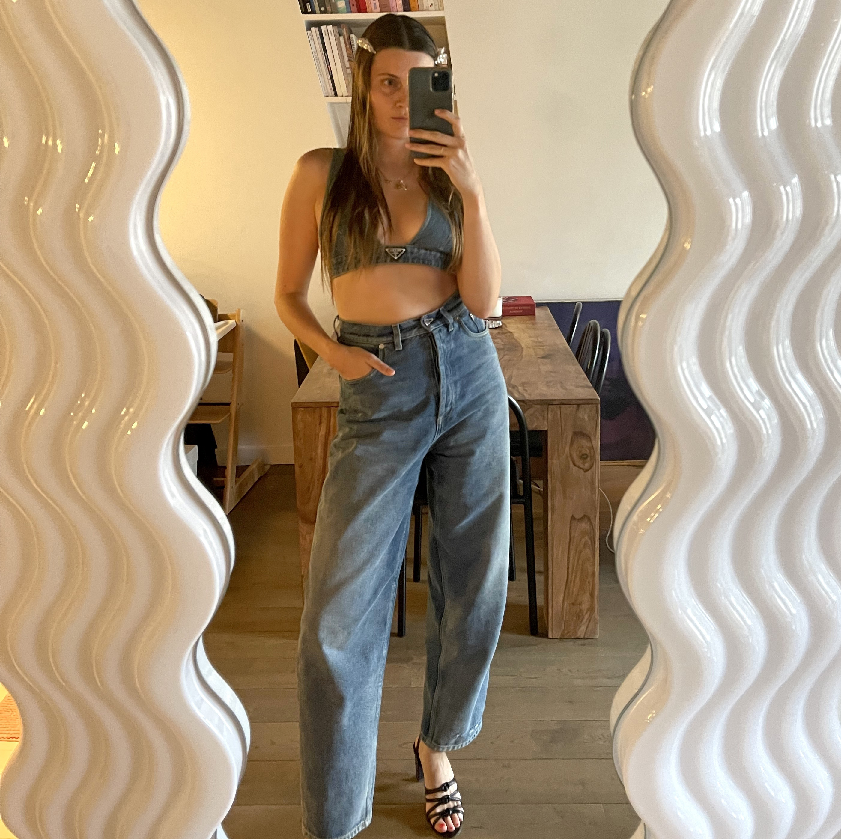 French editor Eugenie Trochu poses in front of an Ettore Sottsass Ultrafragola wavy floor length mirror wearing a denim on denim look
