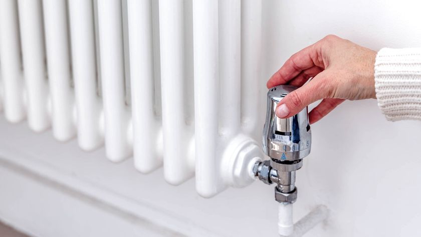 Hand turning chrome TRV on a white column radiator on white wall