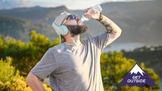 Man drinking from a water bottle while exercising outside surrounded by green trees