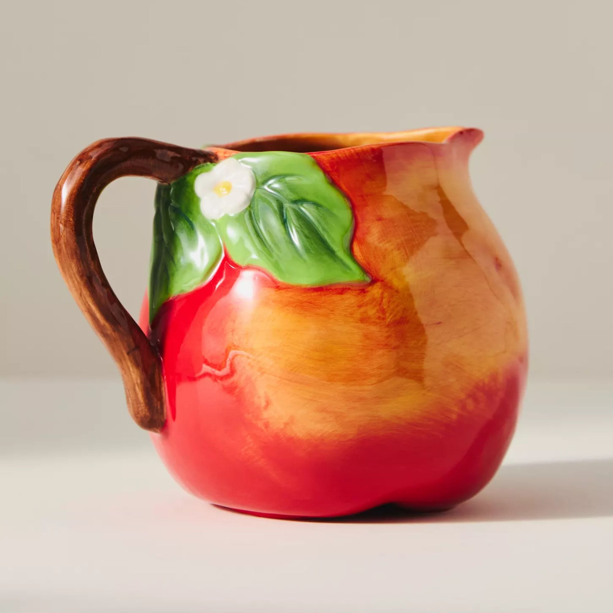 Red jug painted to look like a ripe apple, with green leaves and small daises