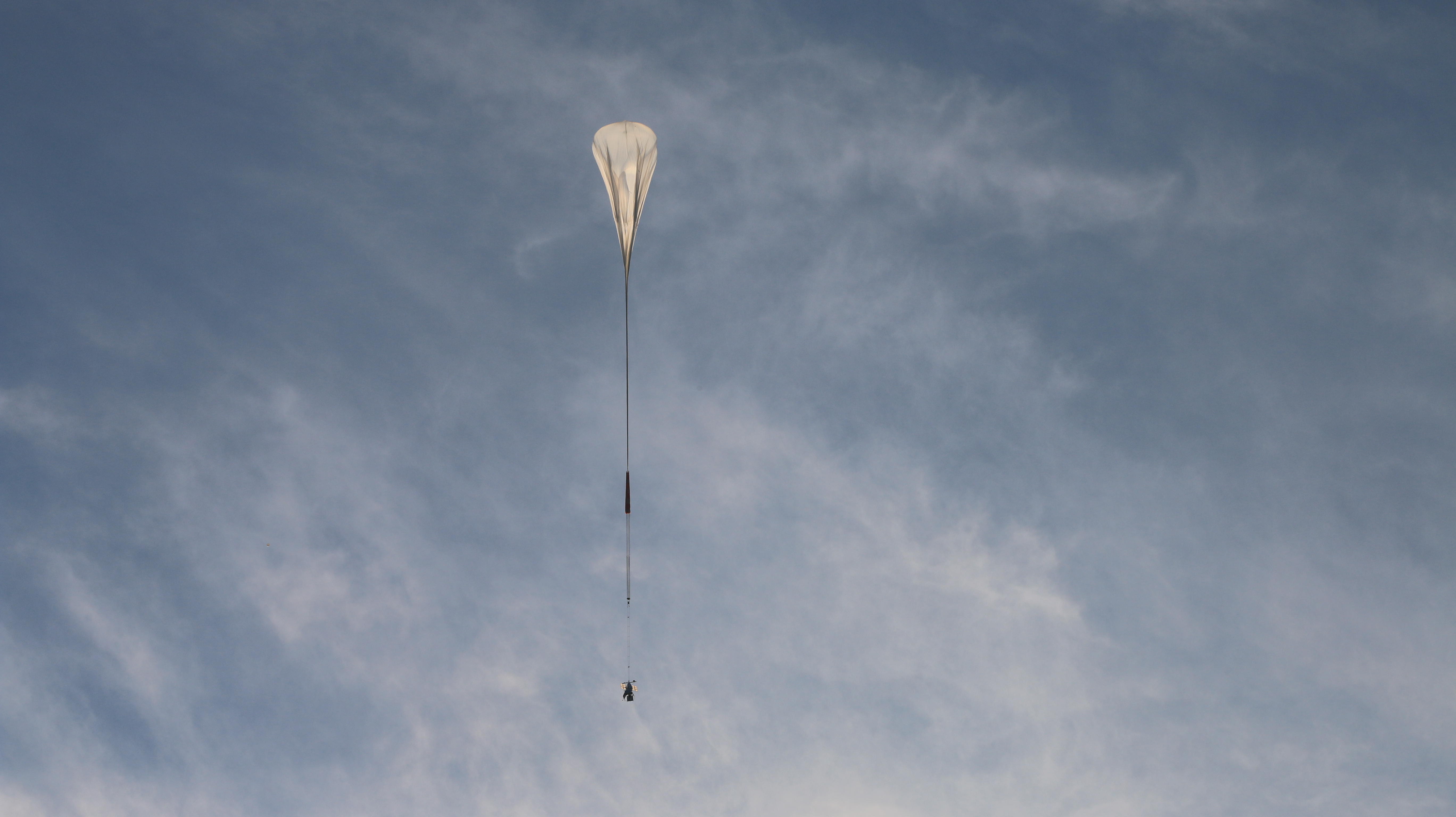 balloon flying in the sky with a long line below it. behind are clouds and a blue sky