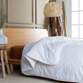 Bed with wooden headboard and white duvet next to window under lampshade