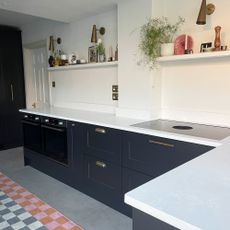 Run of grey kitchen units with white worktops and open shelf instead of wall cabinets