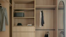 A wood wardrobe with open shelving, hanging clothes and storage drawers alongside a long wall mirror