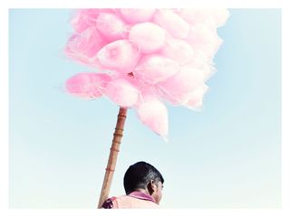 Photo of a person holding a stick with multiple bags of pink candy floss attached under a blue sky