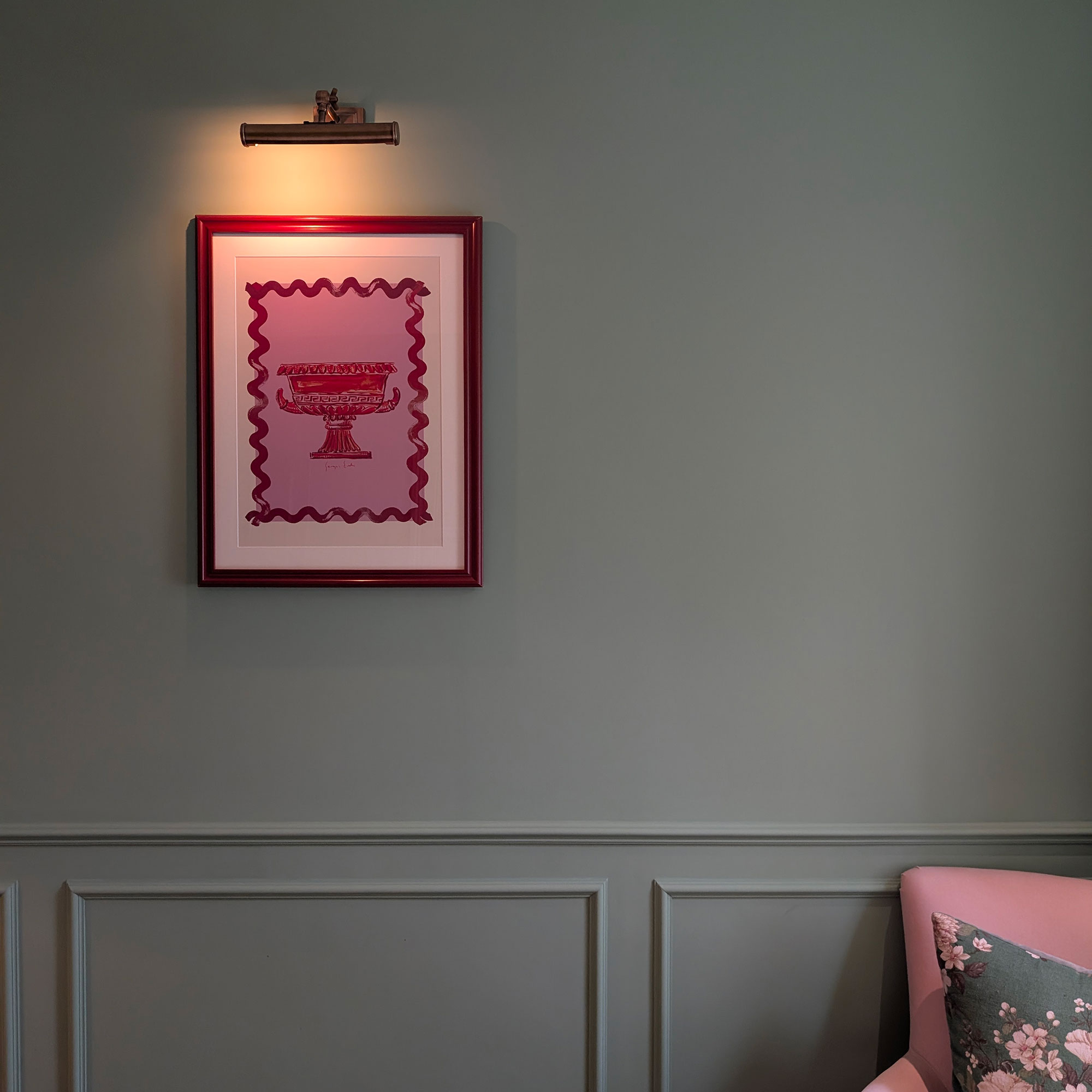 Red framed piece of work under picture light on green panelled wall