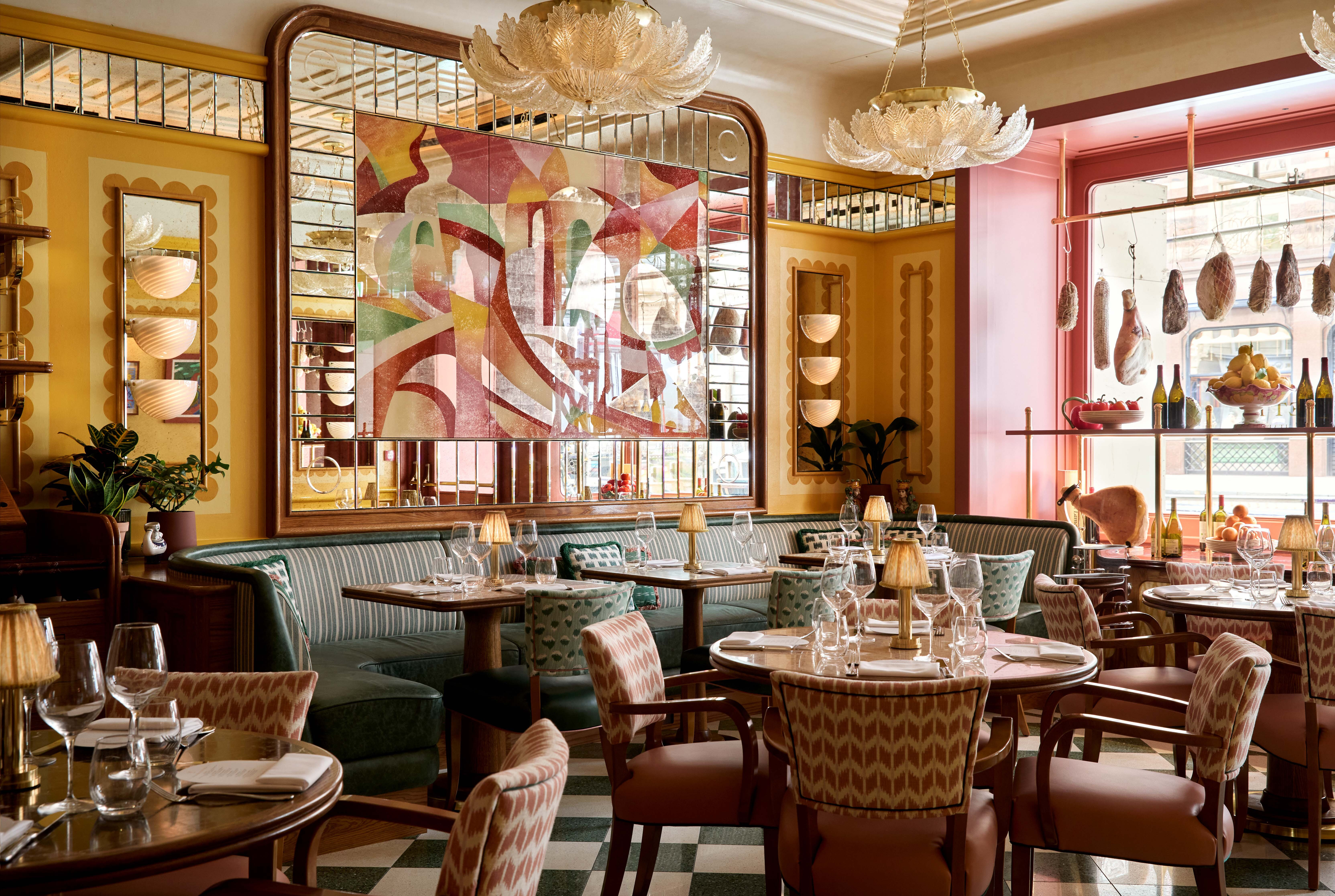 Green banquettes and chairs upholstered in geometric pink patterns inside a yellow-walled restaurant with a huge mirror painted over with abstract pastel shapes