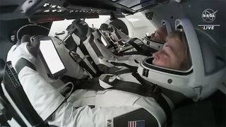 four astronauts in white spacesuits in a cramped capsule