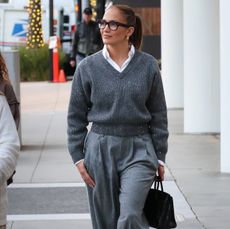 Jennifer Lopez in a gray sweater, trouseres, and glasses.