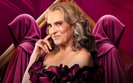 The Traitors Australia season 3 host Gretel Killeen wearing a dark blush read ball gown smiling in foreground, backed by two hooded Traitors 3 contestants in crimson robes