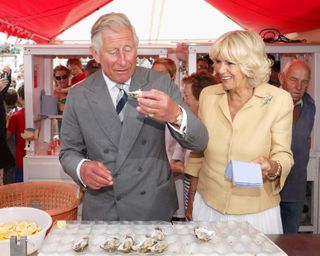 rince Charles, Prince of Wales eats an oyster as Camilla, Duchess of Cornwall looks on during their visit to the Whitstable Oyster Festival on July 29, 2013 in Whitstable, England. (Photo by Max Mumby/Indigo/Getty Images)