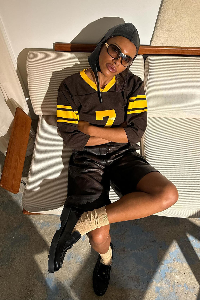 A woman wearing a brown and yellow jersey, leather shorts, and loafers