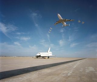 The space shuttle Enterprise is seen on the Edwards Air Force Base runway with the Shuttle Carrier Airfract and NASA jets in the flying overhead in this September 1977 image.